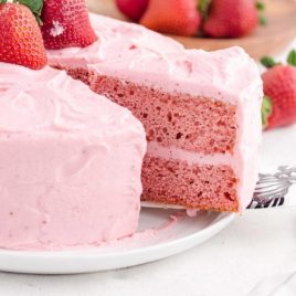 close up side shot of strawberry cake with a slice being taken out of it with a spatula