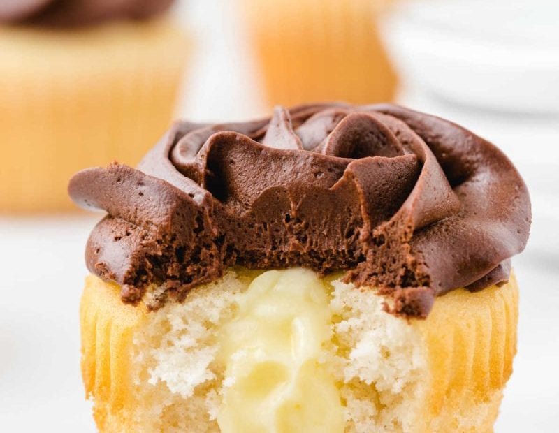 boston cream cupcakes with chocolate frosting with a bite taken out of it showing its cream cheese filling inside
