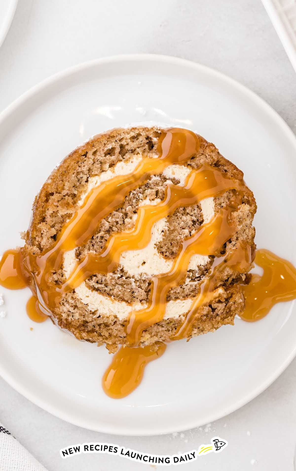 overhead shot of a slice of caramel banana cake roll drizzled with caramel sauce on a plate