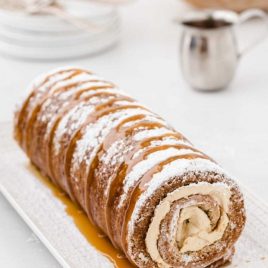 caramel banana cake roll drizzled with caramel sauce and dusted with powdered sugar on a plate