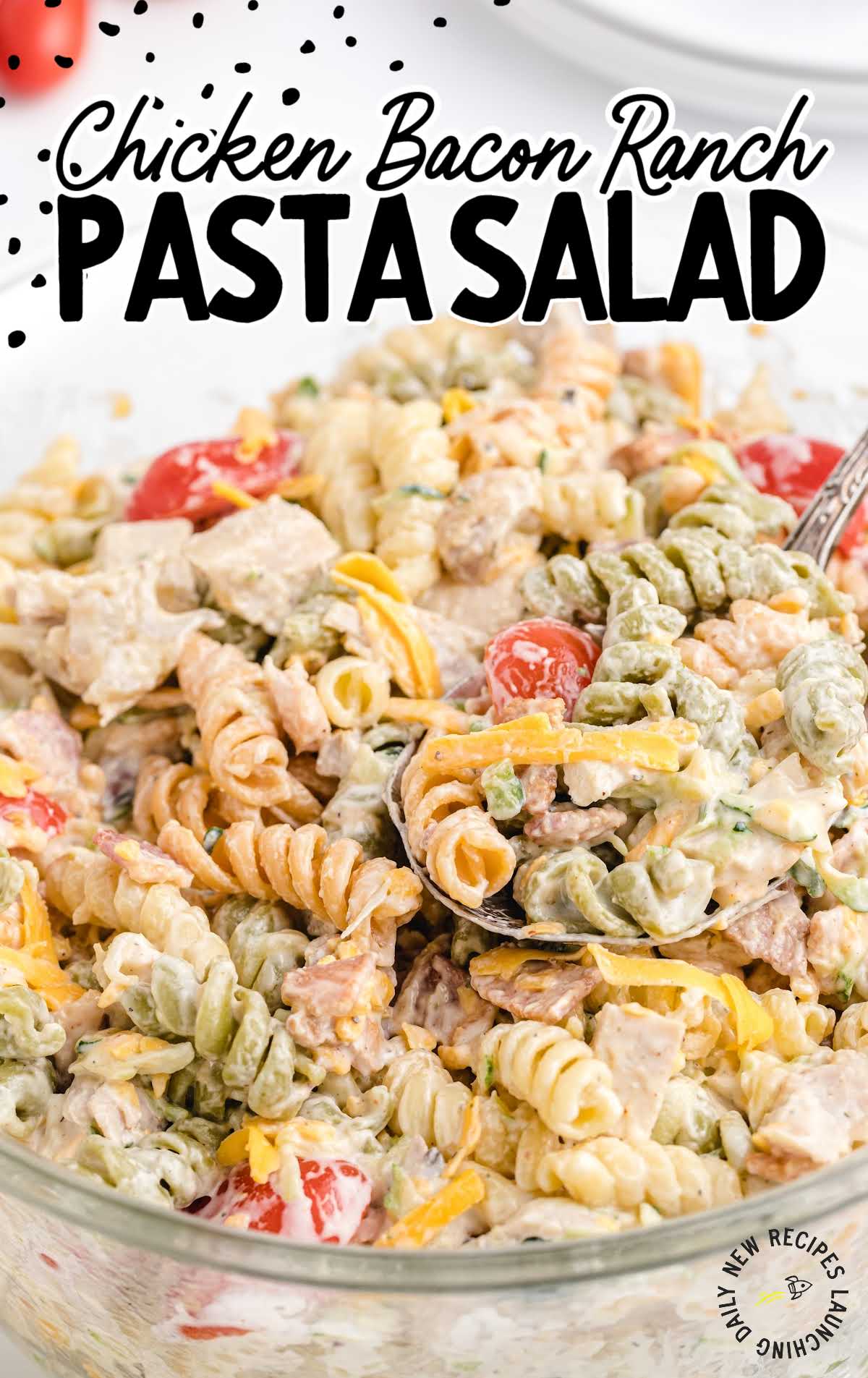 Spoon scooping chicken bacon ranch pasta salad from a large bowl with visible pasta, bacon, and cherry tomatoes.