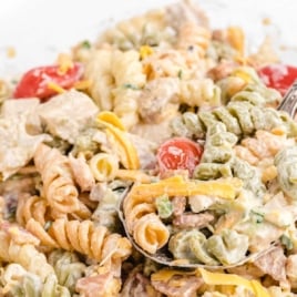 Close-up of creamy chicken bacon ranch pasta salad in a clear bowl with rotini, tomatoes, bacon, and cheese.