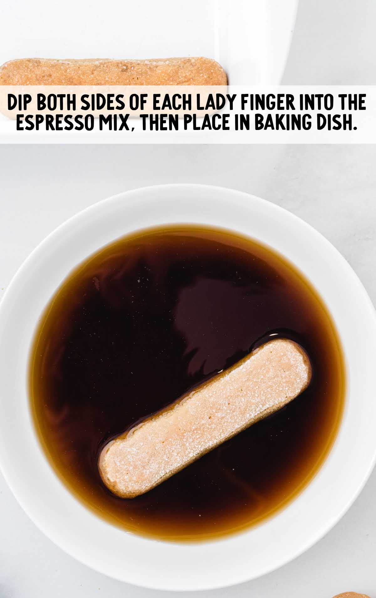 Ladyfinger being dipped into a bowl of espresso mixture as part of tiramisu assembly instructions