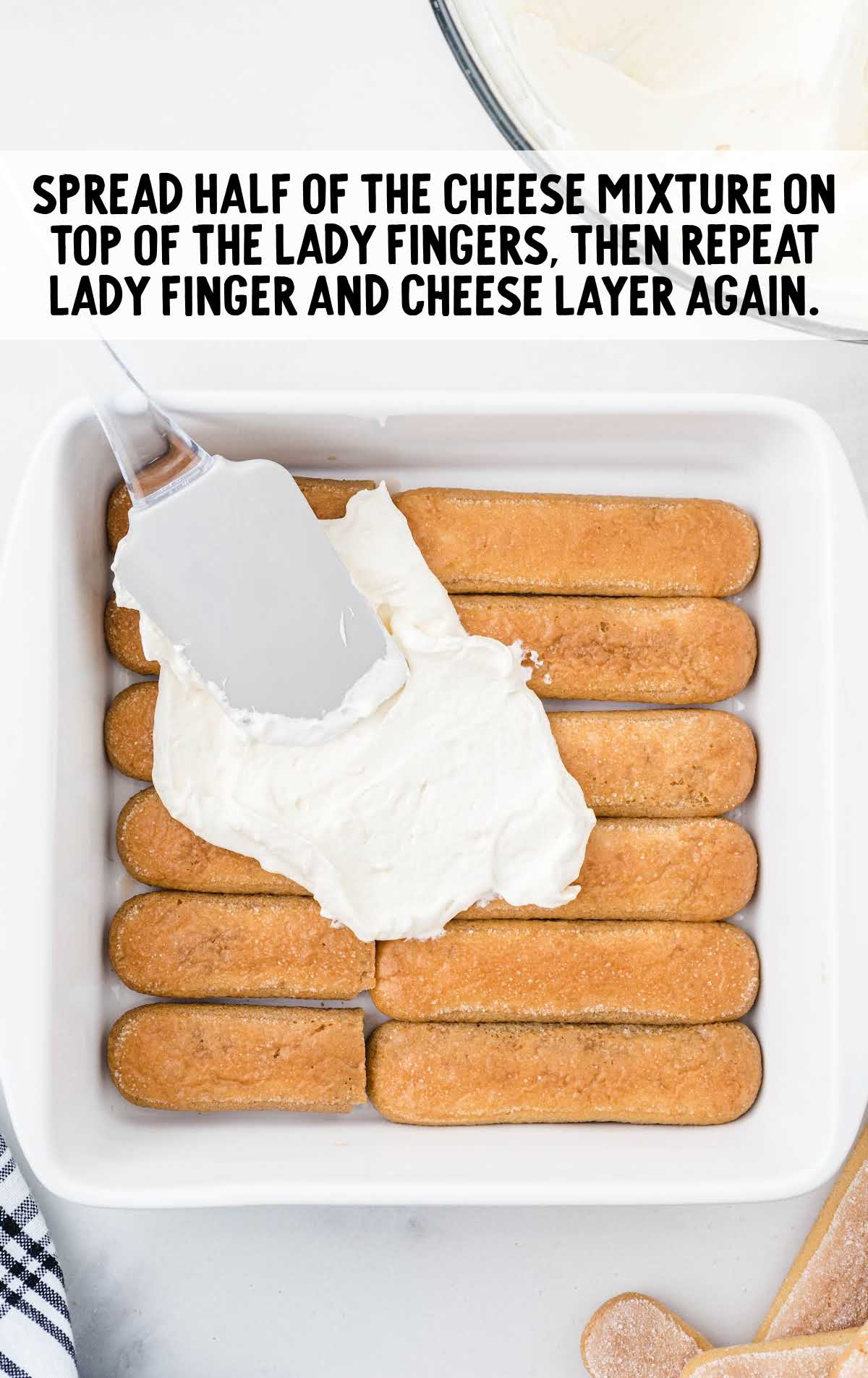 Spreading mascarpone cheese mixture over ladyfingers in a white baking dish for tiramisu layer