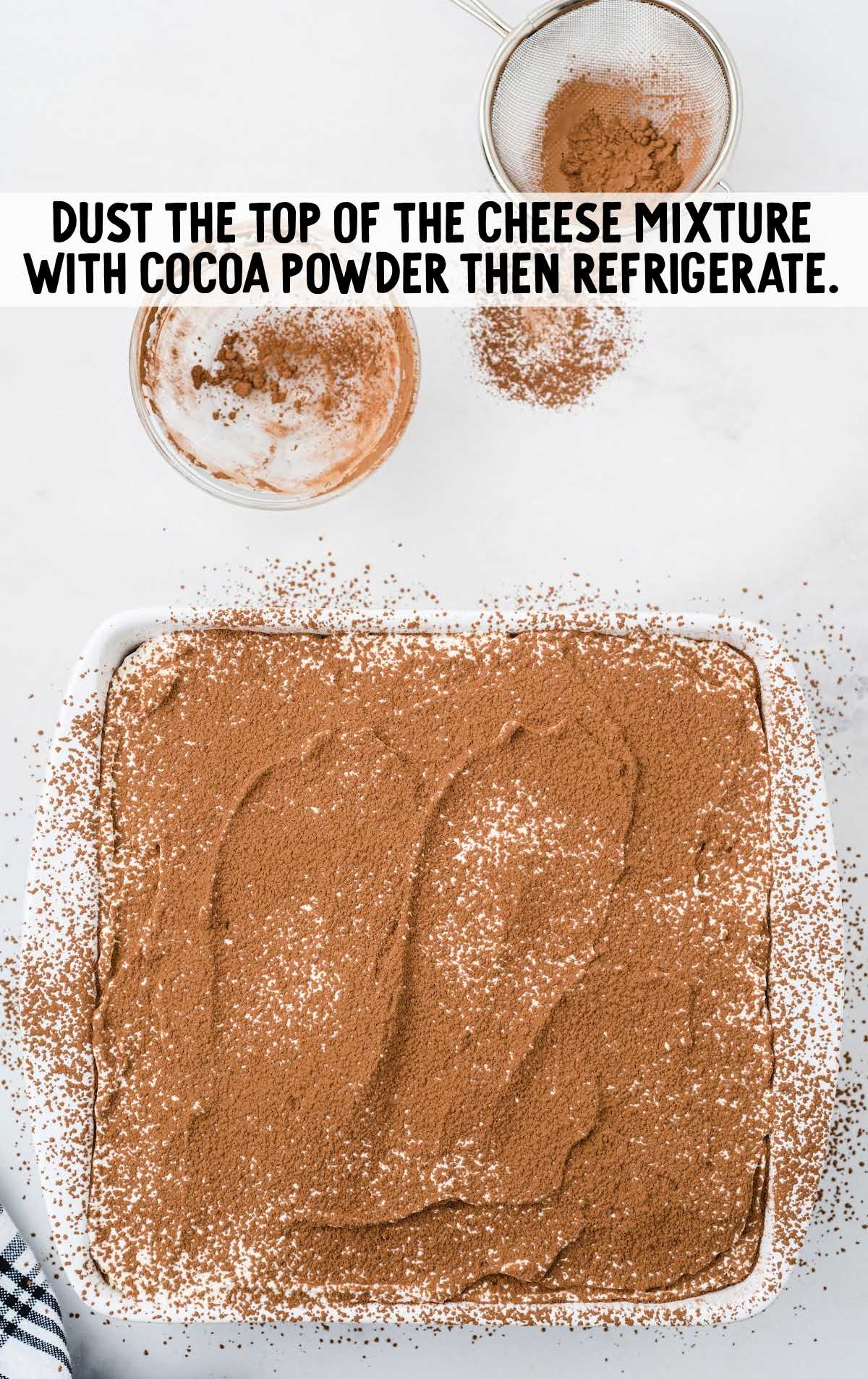 Top-down view of tiramisu being dusted with cocoa powder using a mesh strainer, final step before refrigeration