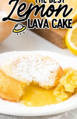 close up shot of lemon lava cake dusted with powdered sugar with a bite taken out showing its inside lemon layers on a white plate with lemon slices in the back