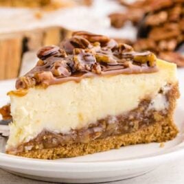 a slice of pecan pie cheesecake topped with caramel and pecans on a white plate