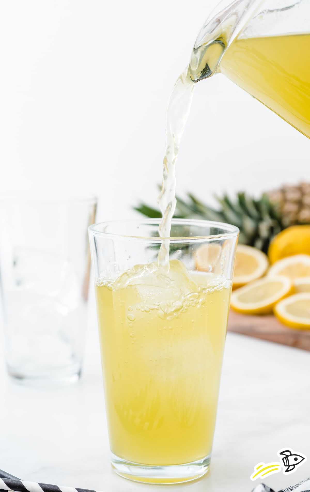 a pitcher of pineapple lemonade being poured into a glass of ice