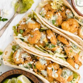 overhead shot of shrimp tacos with spicy cilantro lime sauce topped with cilantro and feta cheese with limes on the side
