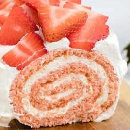 strawberry roll cake garnished with diced strawberries on a wooden board