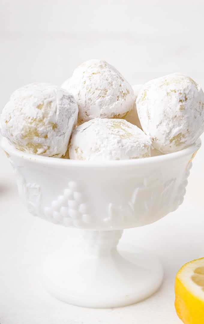 close up shot of white chocolate lemon truffles dipped into powdered sugar in a bowl