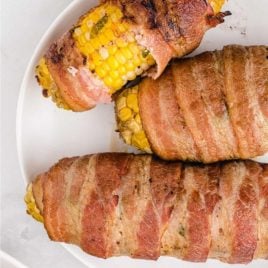 overhead shot of bacon-wrapped corn on the cob on a white plate
