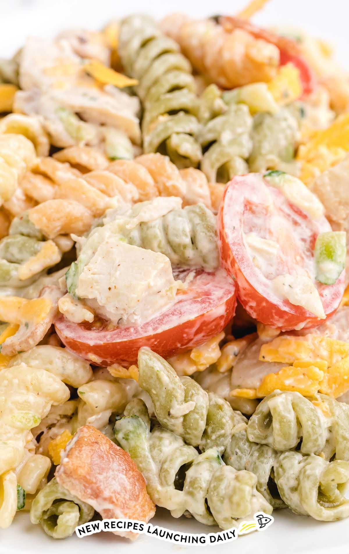 Close-up of a serving of chicken bacon ranch pasta salad on a white plate showing creamy dressing and fresh ingredients.