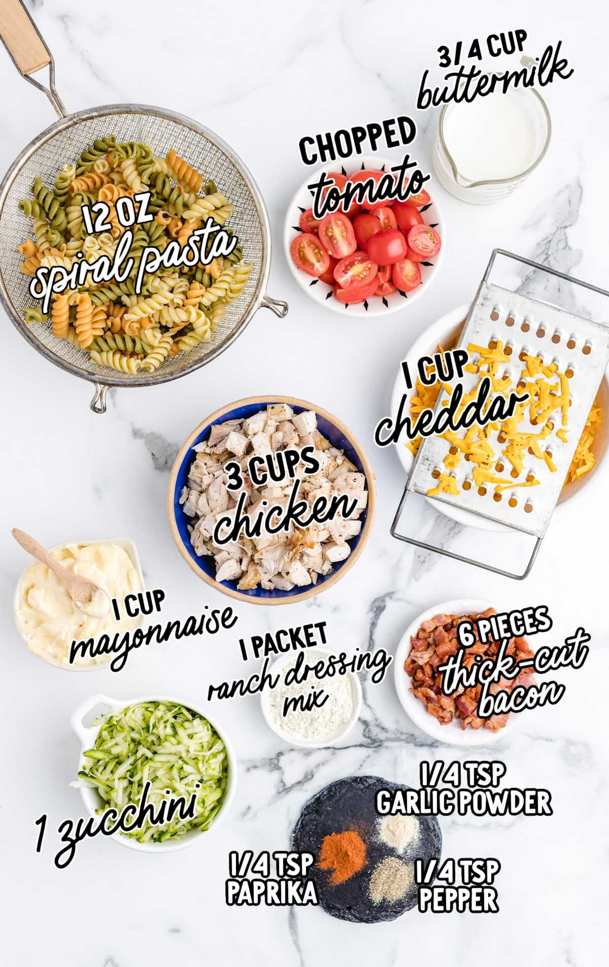 Flat lay of chicken bacon ranch pasta salad ingredients including spiral pasta, chicken, bacon, cheddar, zucchini, and seasonings.
