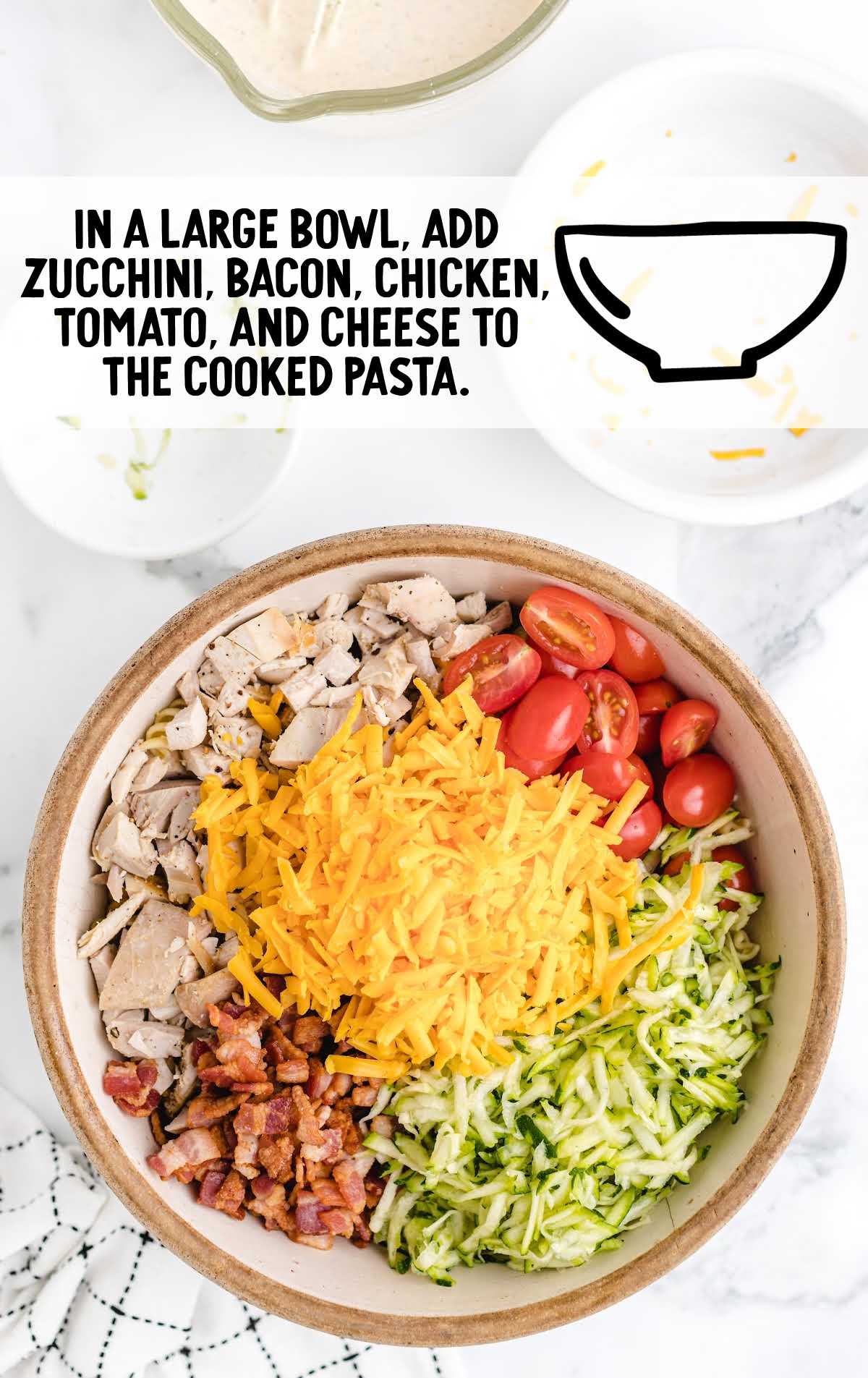 Bowl with shredded zucchini, bacon, chopped chicken, tomatoes, and cheddar before mixing with pasta.