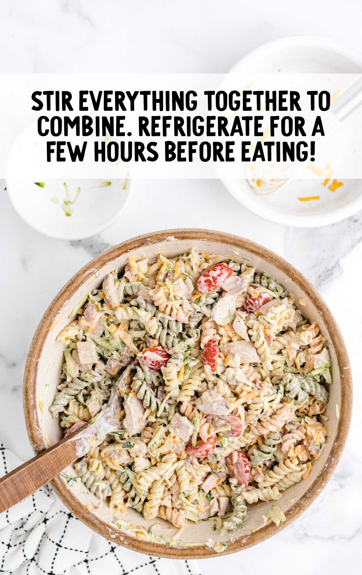 Mixed chicken bacon ranch pasta salad in a large bowl with wooden spoon ready to chill before serving.