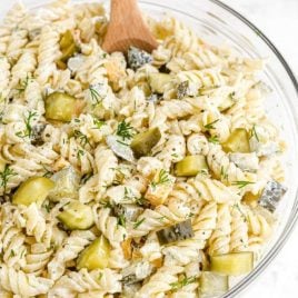 close up overhead shot of dill pickle pasta salad in a clear bowl with a large wooden spoon