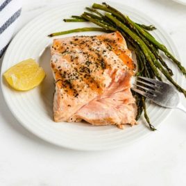 close up shot of grilled salmon on a plate with asparagus and a slice of lemon