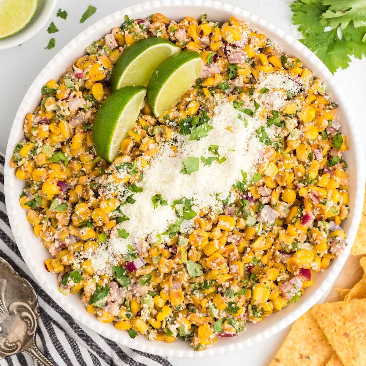 close up overhead shot of Mexican corn salad garnished with parsley then topped with Cotija cheese and lime slices