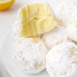 close up shot of white chocolate lemon truffles dipped into powdered sugar with a bite taken out of one on a plate