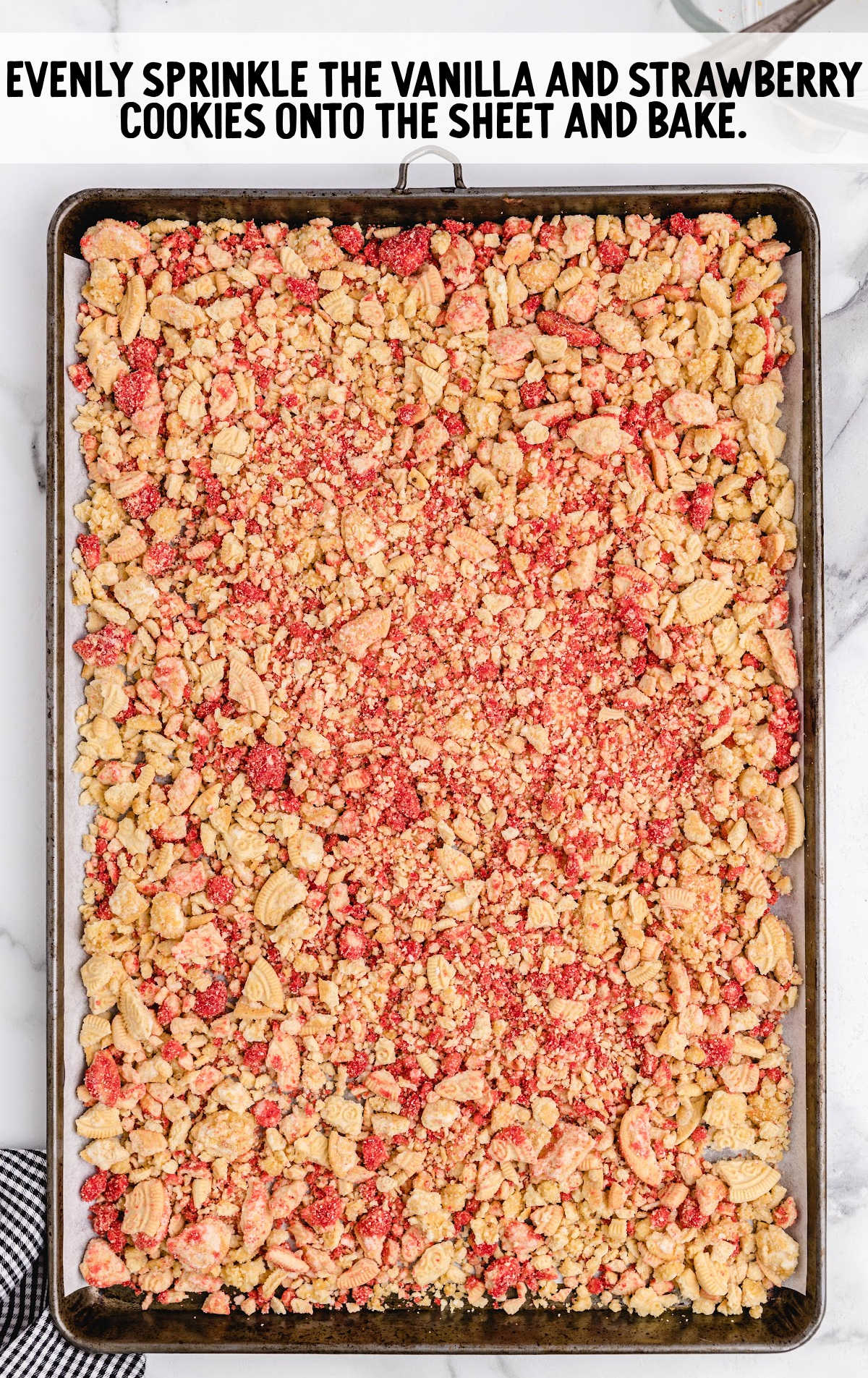Crumbled vanilla and strawberry cookie mixture spread evenly on a baking sheet, ready for baking.