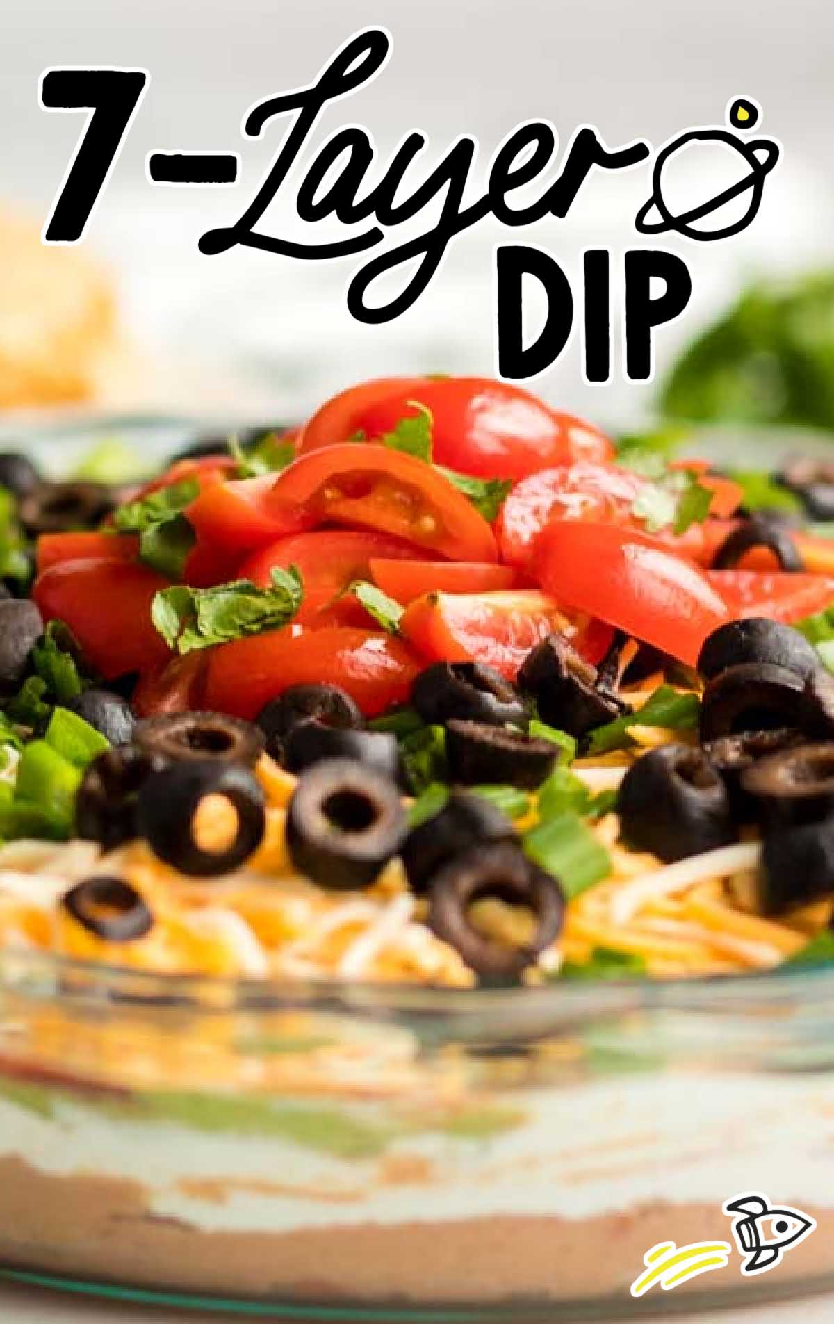 close up shot of a bowl of seven layer dip topped with sliced tomatoes, green onions, and black olives