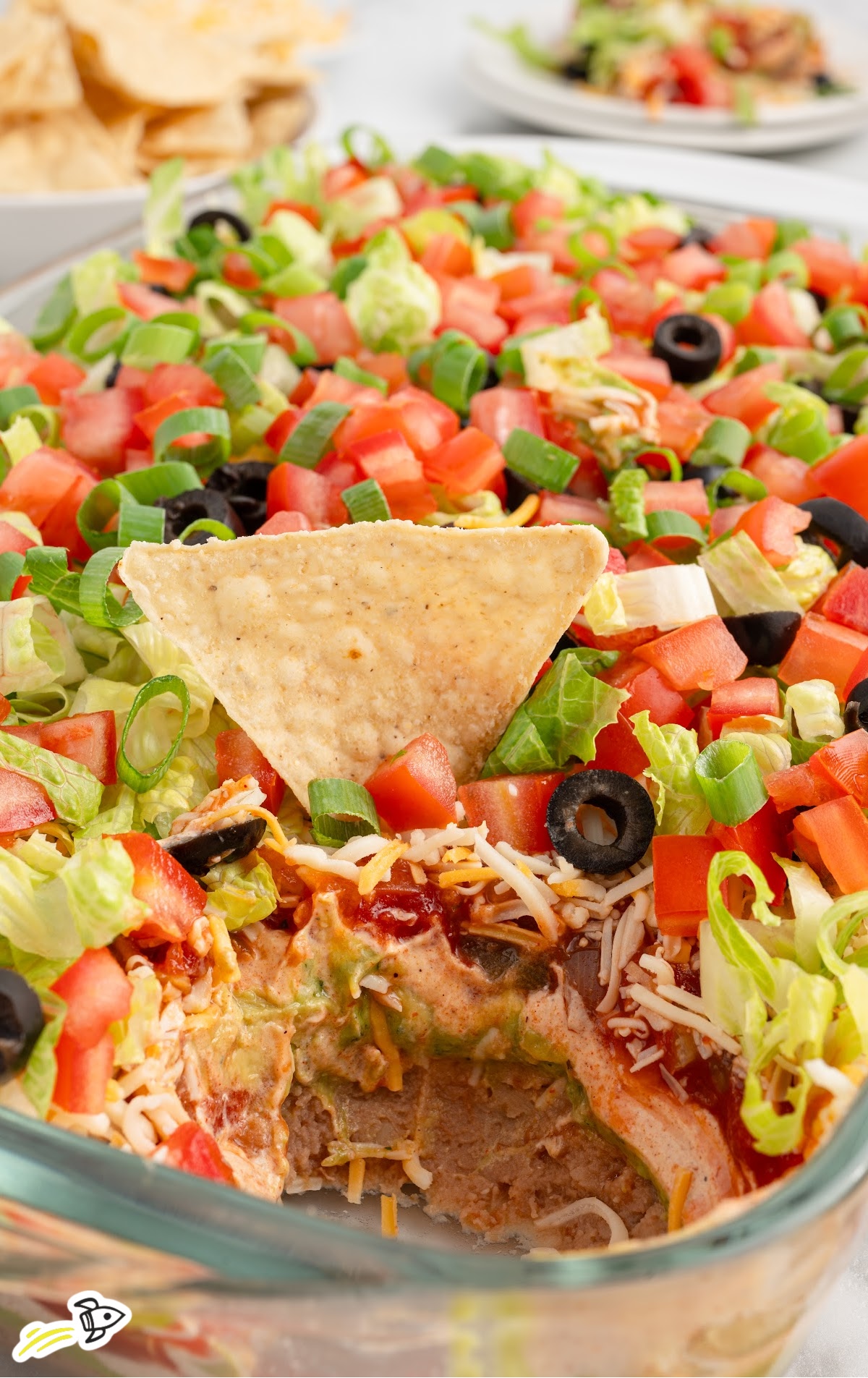 a baking dish of 7 Layer Dip with a tortilla chip