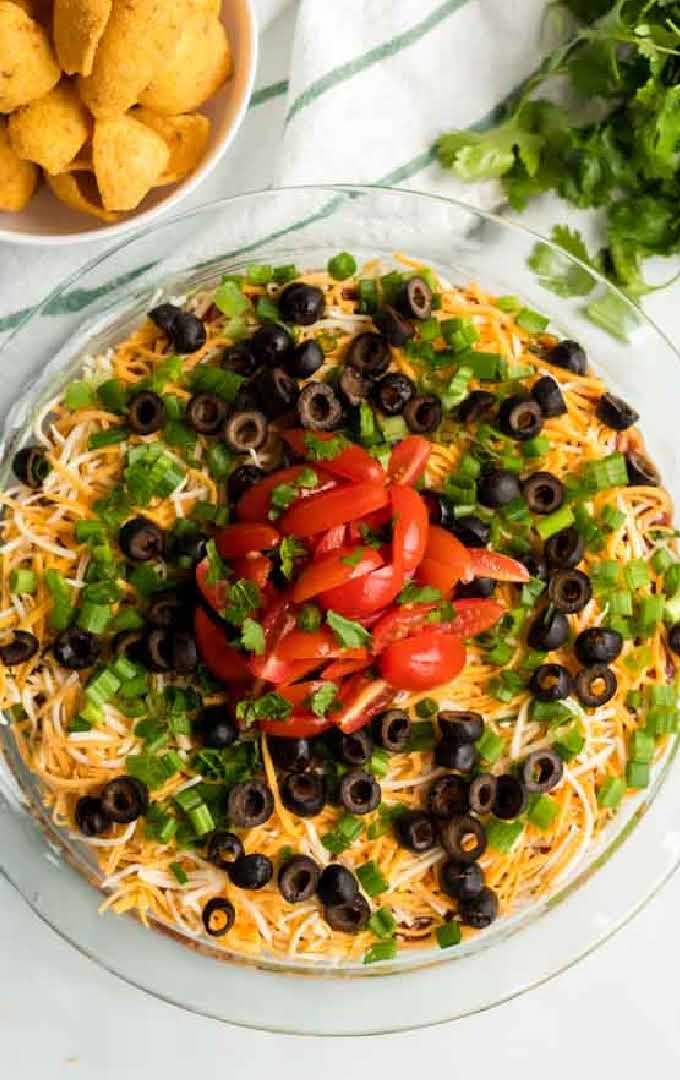 close up overhead shot of a bowl of seven layer dip topped with sliced tomatoes, green onions, and black olives