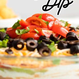 close up shot of a bowl of seven layer dip topped with sliced tomatoes, green onions, and black olives