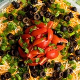 overhead shot of a bowl of seven layer dip topped with sliced tomatoes, green onions, and black olives