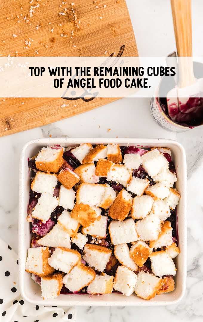 blueberry angel food cake process shot of remaining cubes of angel cake being placed over pie filling in a baking dish