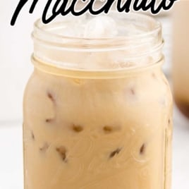 A mason jar filled with iced caramel macchiato sits on a white surface. Black text above and below the jar reads “The Best Iced Caramel Macchiato Recipe Homemade!”.