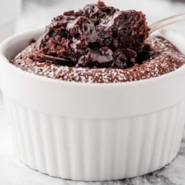 Close-up of warm chocolate lava cake in a white ramekin with a rich molten center and a spoonful lifted.