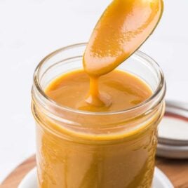 close up shot of Carolina mustard BBQ sauce in a mason jar with the sauce being picked up with a spoon