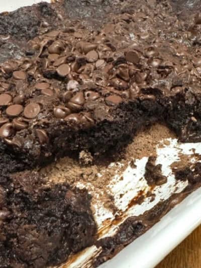 Partially eaten Chocolate Dump Cake in a white baking dish, topped with melted chocolate chips and rich chocolate frosting, showing a gooey and moist texture.