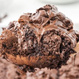 A close-up of a gooey chocolate lava cake, inspired by a classic Chocolate Dump Cake Recipe, being lifted from a baking dish with a wooden spoon, showing melted chocolate and a rich, moist texture.