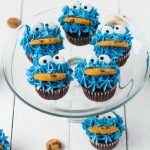close up shot of Cookie Monster Cupcakes with candy eyes and a cookie on a clear serving stand