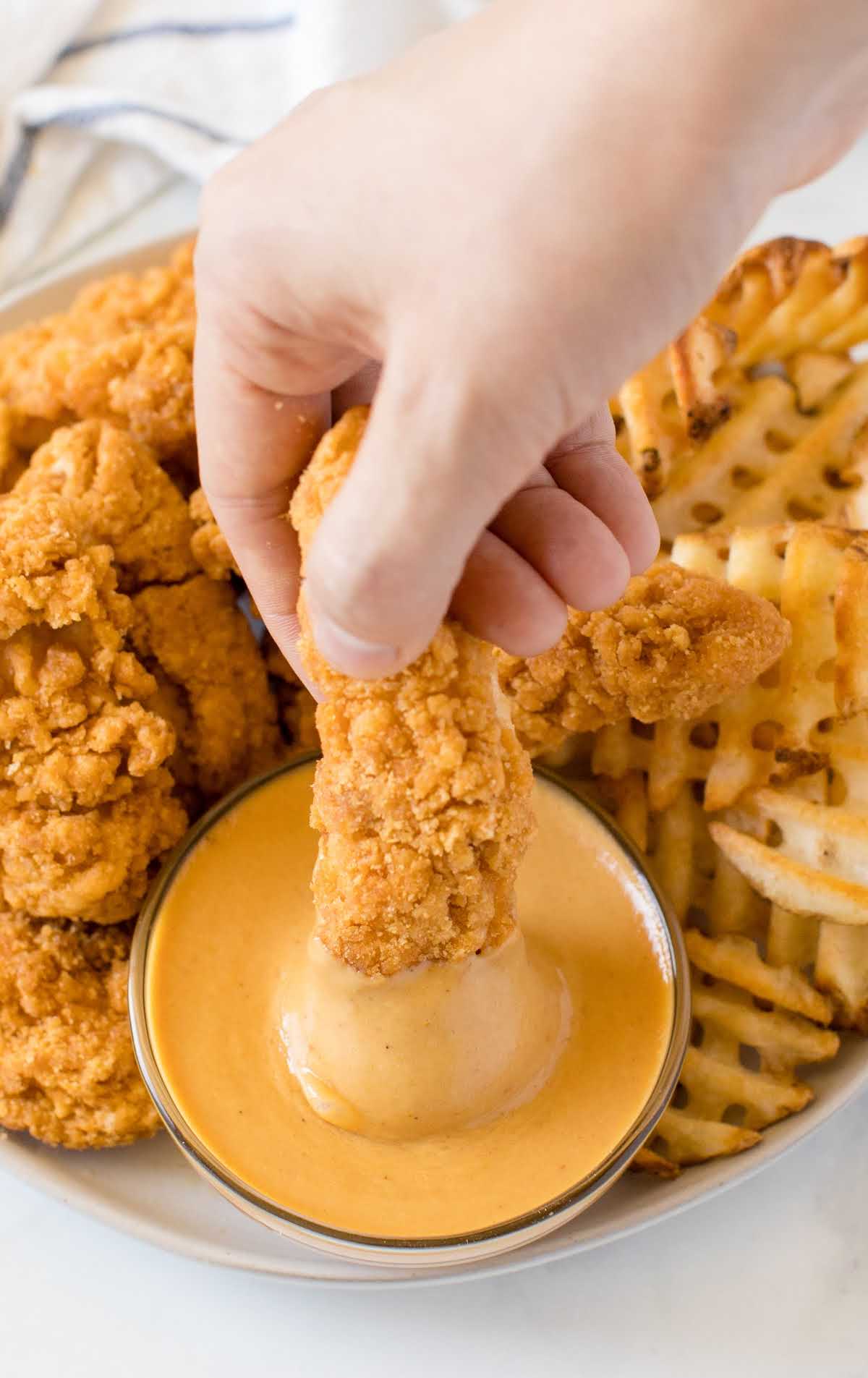 close up shot of copycat chick fil a sauce in a condiment cup with chicken tenders and fries