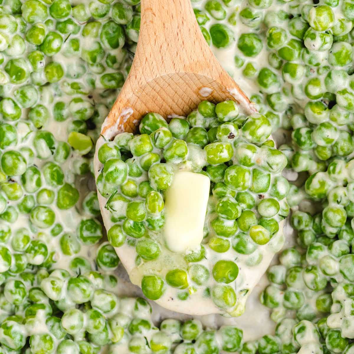 Close-up of wooden spoon filled with creamy peas and melting butter.