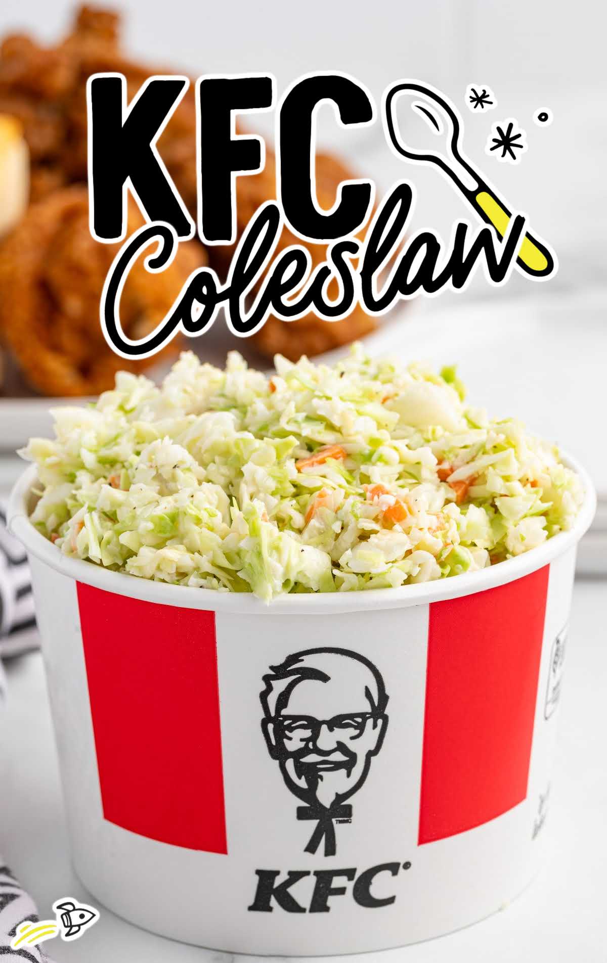 Large container of KFC copycat coleslaw with bold “KFC Coleslaw” text and fried chicken blurred in the background.