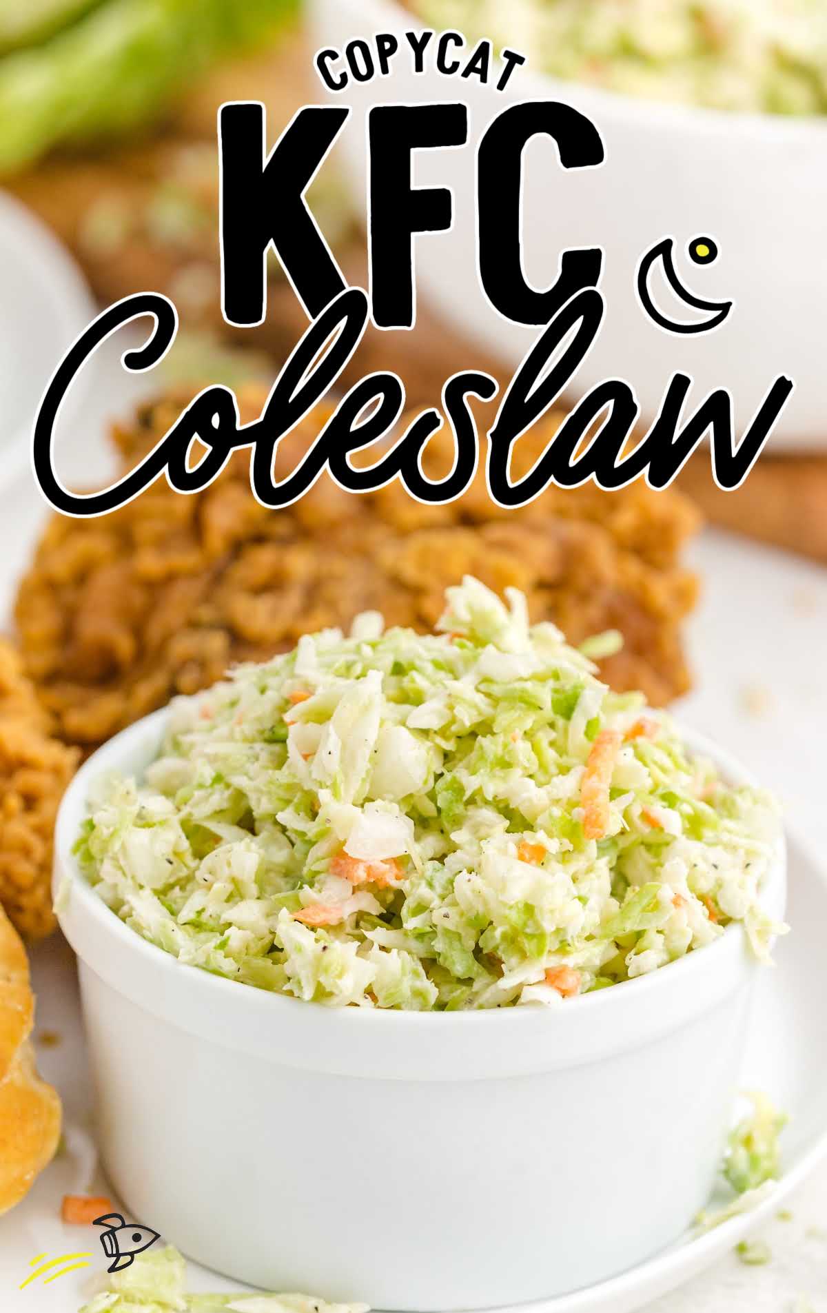 White bowl of coleslaw labeled as “Copycat KFC Coleslaw” with fried chicken and biscuit in the background.