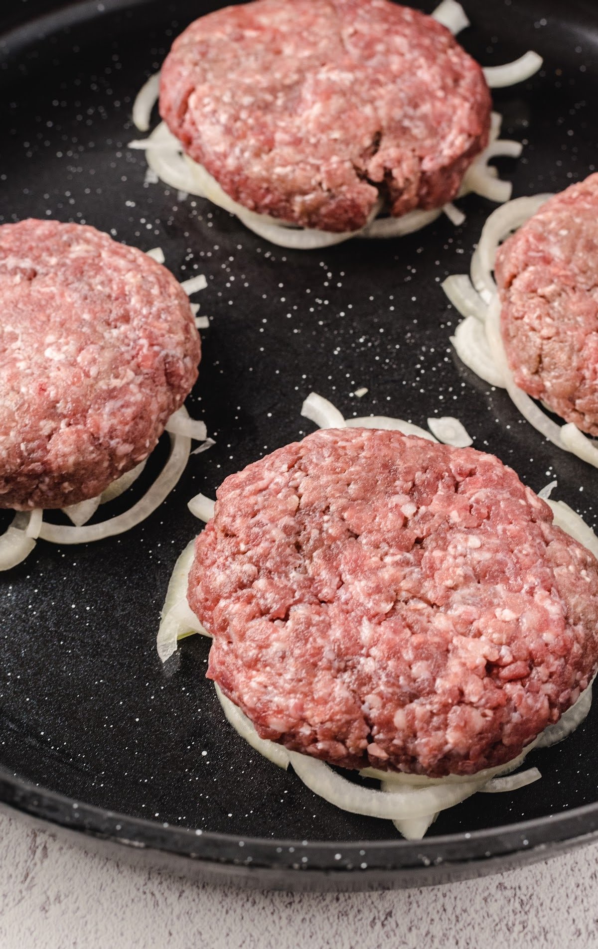 ground beef patties on top of cut onions on a skillet