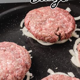 ground beef patties on top of cut onions on a skillet