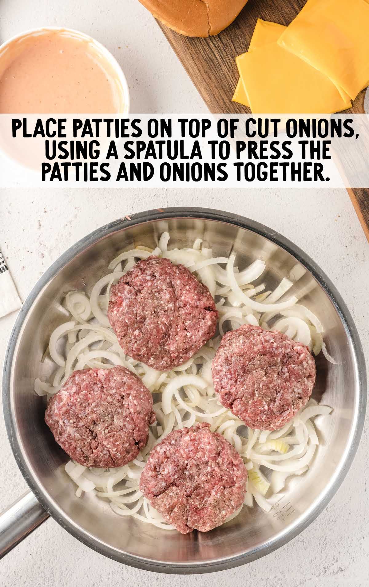 raw burgers laid on top of cut onions on a skillet