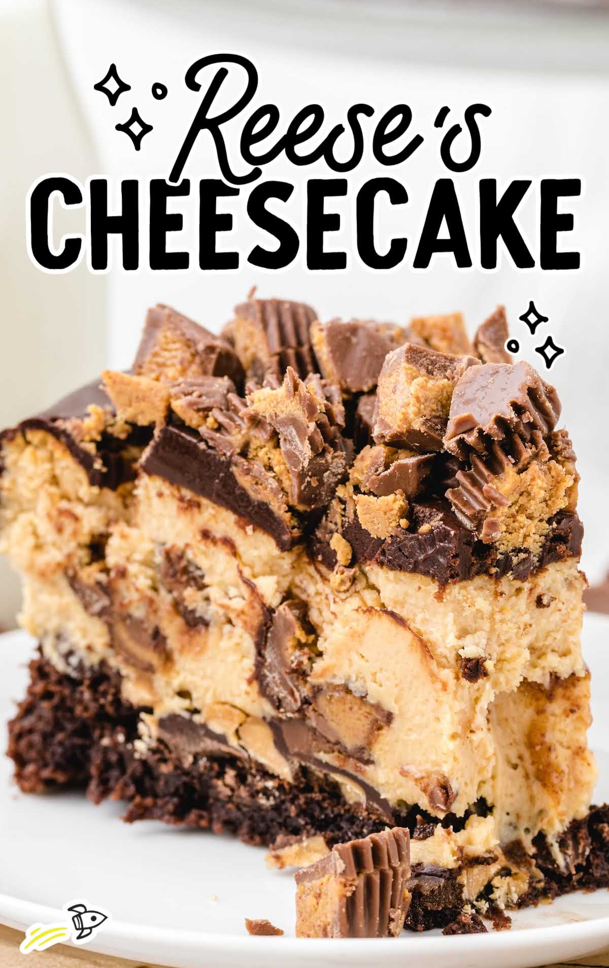 Slice of Reese’s cheesecake labeled “Reese’s Cheesecake,” showing chocolate, peanut butter filling, and candy topping.
