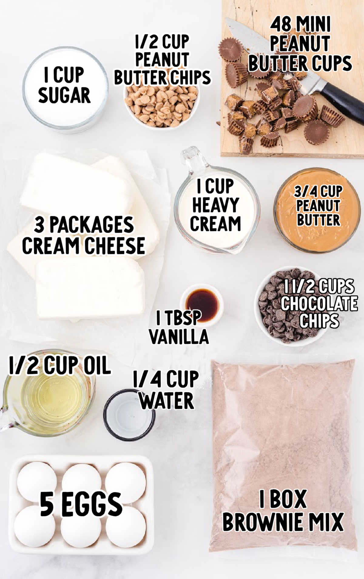 Overhead layout of ingredients for Reese’s cheesecake, including peanut butter, brownie mix, eggs, cream cheese, chocolate chips, and peanut butter cups.