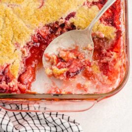 close up shot of Strawberry Cobbler slice missing in a baking dish with a spoon