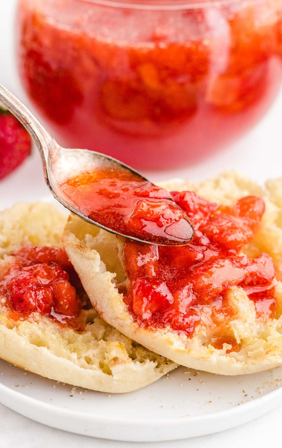 close up shot of strawberry freezer jam being poured on top bread with a spoon on a plate