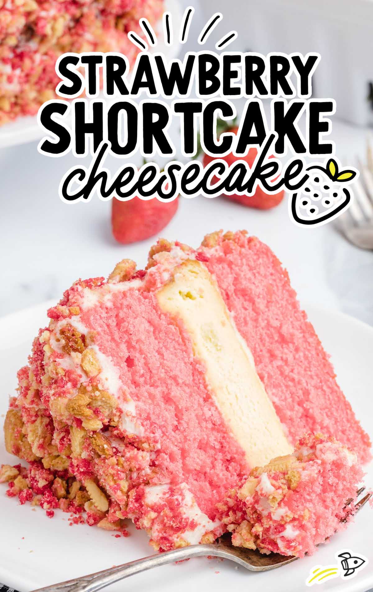 Slice of strawberry shortcake cheesecake on a white plate with text overlay and strawberries in background.