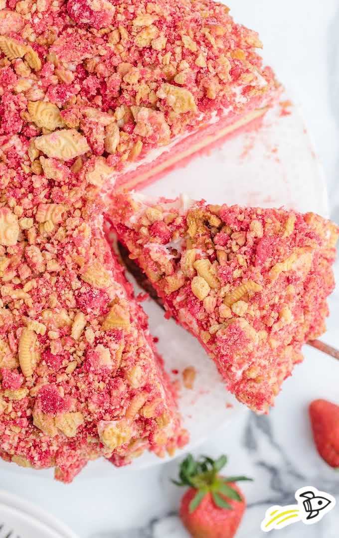 Overhead view of a sliced strawberry shortcake cheesecake topped with cookie crumbles, with one slice being lifted.